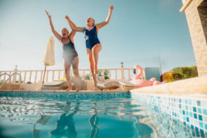 Two women holding hands and jumping into a swimming pool. They're excited and having fun.